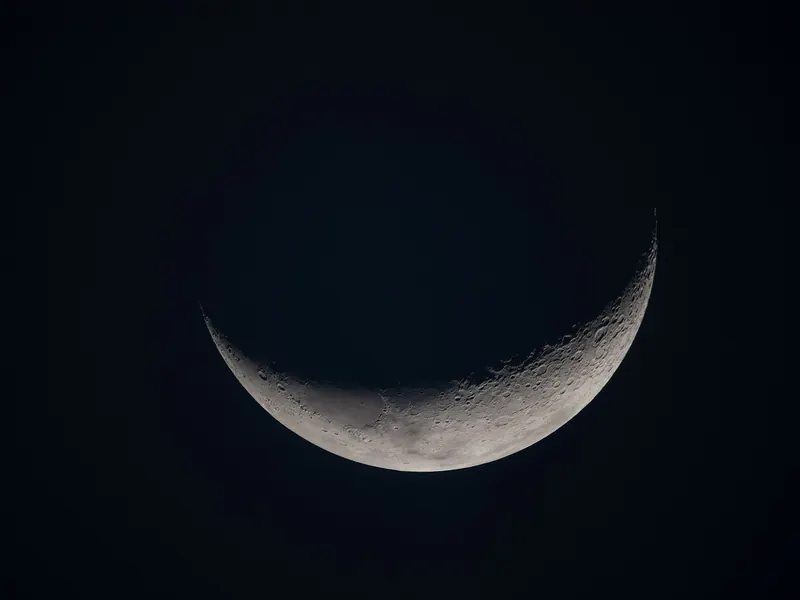 A thin crescent Moon glowing against black space