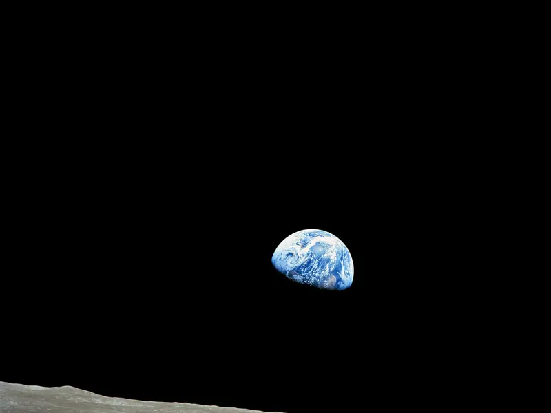 Earth, half lit and blue, rising above the grey edge of the Moon against black space